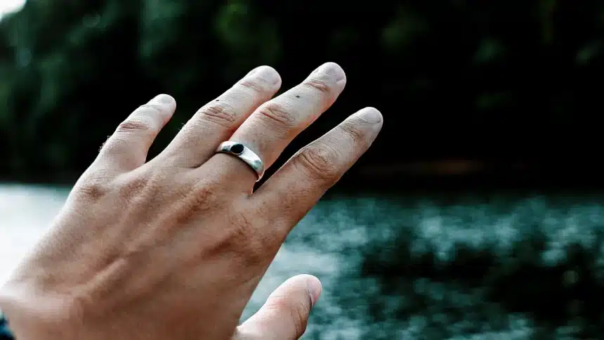 Hand wearing a smart ring near water.