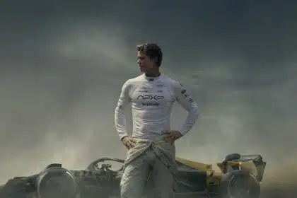 Brad Pitt standing in front of a Formula 1 race car on a dusty track.