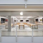 Apple retail store in the UK with product displays and large wall screens.