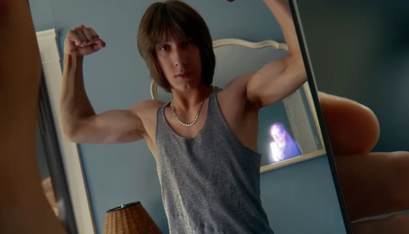 Man flexing in mirror with photographer’s reflection in background.