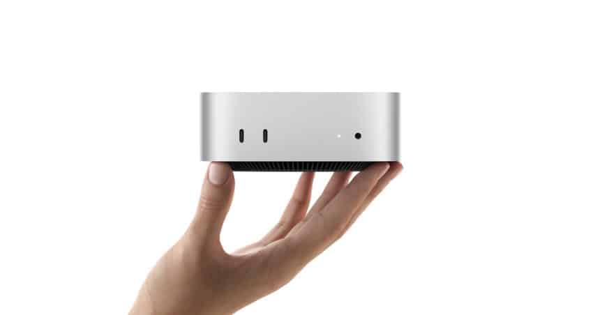 A hand holding a silver Apple Mac mini computer.