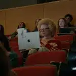 Student using iPhone and MacBook with accessibility tools in a lecture hall.