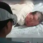 Woman wearing Apple Vision Pro watches a 3D video of a newborn baby.