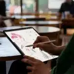 Person drawing on an iPad with Apple Pencil in a café setting.