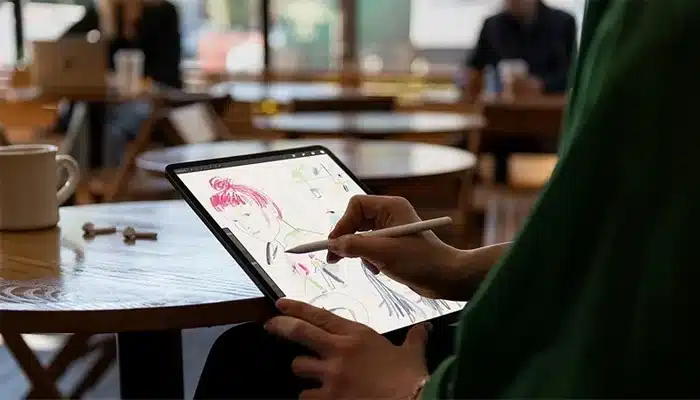 Person drawing on an iPad with Apple Pencil in a café setting.