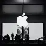 Silhouettes of people inside an Apple Store with a large Apple logo overhead.