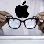 Person holding Apple smart glasses with digital data reflected in the lenses.