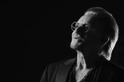Bono in a black-and-white portrait wearing glasses and a dark jacket.