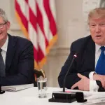Tim Cook and Donald Trump seated at a meeting, speaking with microphones.