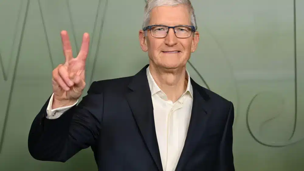 Tim Cook flashes a peace sign while wearing a suit and glasses.