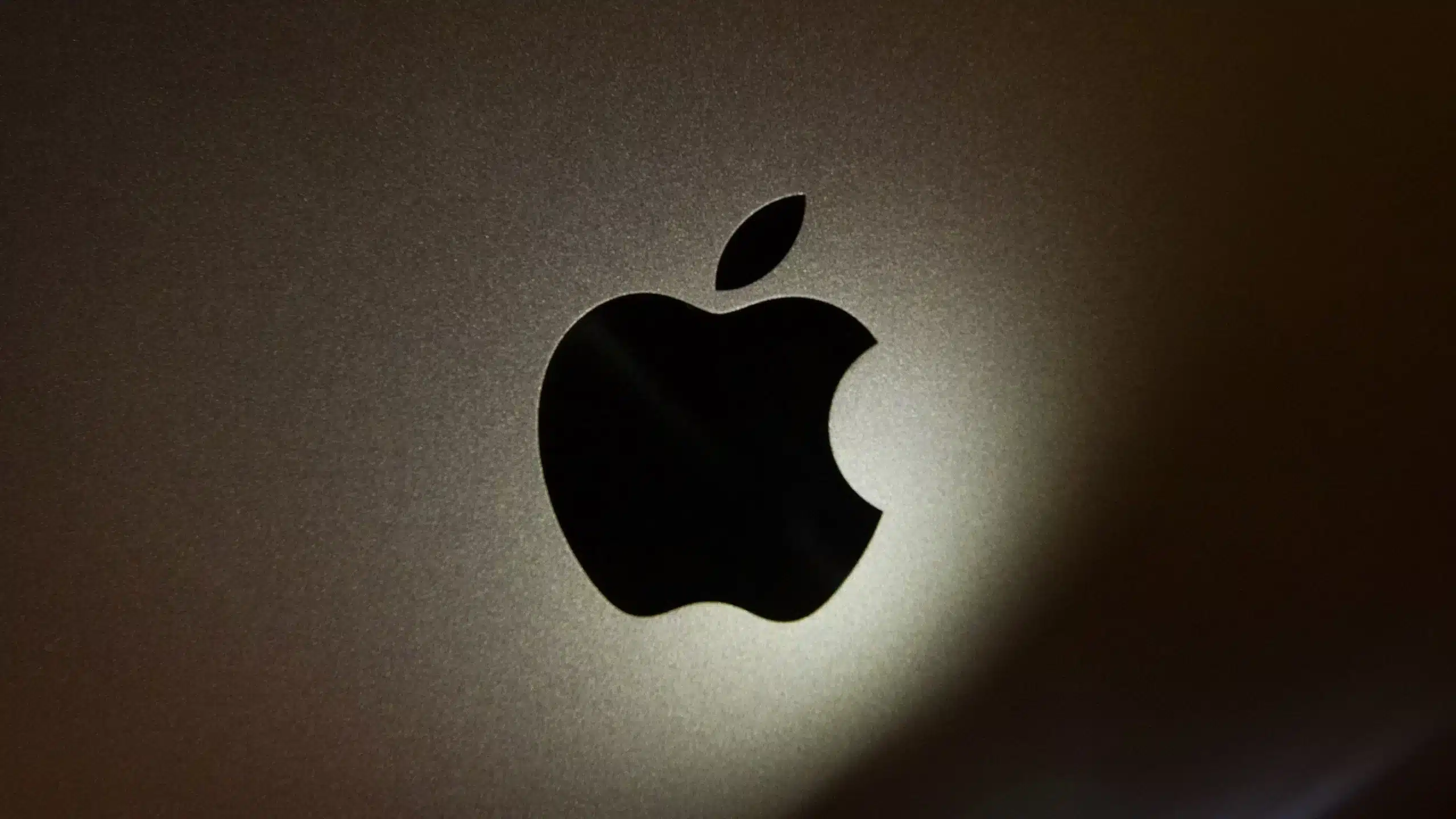 Close-up of a black Apple logo on a metallic surface with soft lighting.