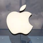 Apple logo on glass building facade with reflections of clouds.