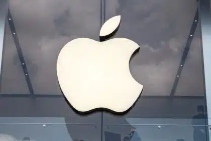 Apple logo on glass building facade with reflections of clouds.