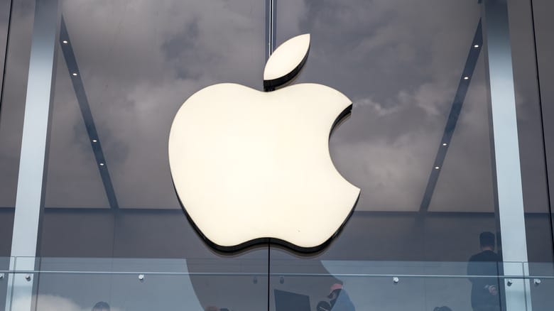 Apple logo on glass building facade with reflections of clouds.