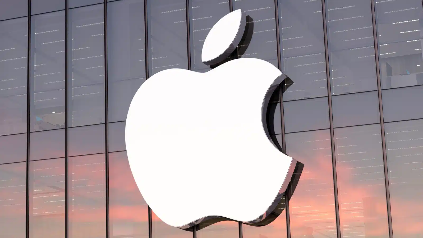 Apple logo on the glass exterior of a corporate building during sunset.