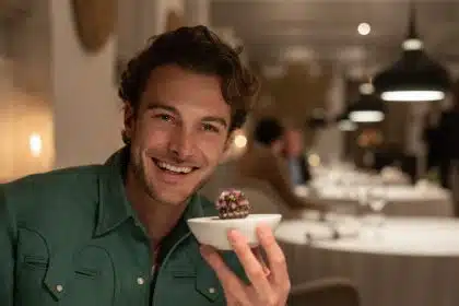 Man smiling and holding a small gourmet dish in a fine dining restaurant.