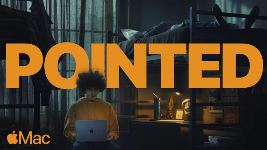 A student in a hoodie uses a MacBook in a dimly lit dorm room with the word "POINTED" in bold text.