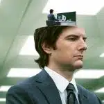 A man in a suit with a miniature version of himself working at a desk inside his head, from the show Severance.