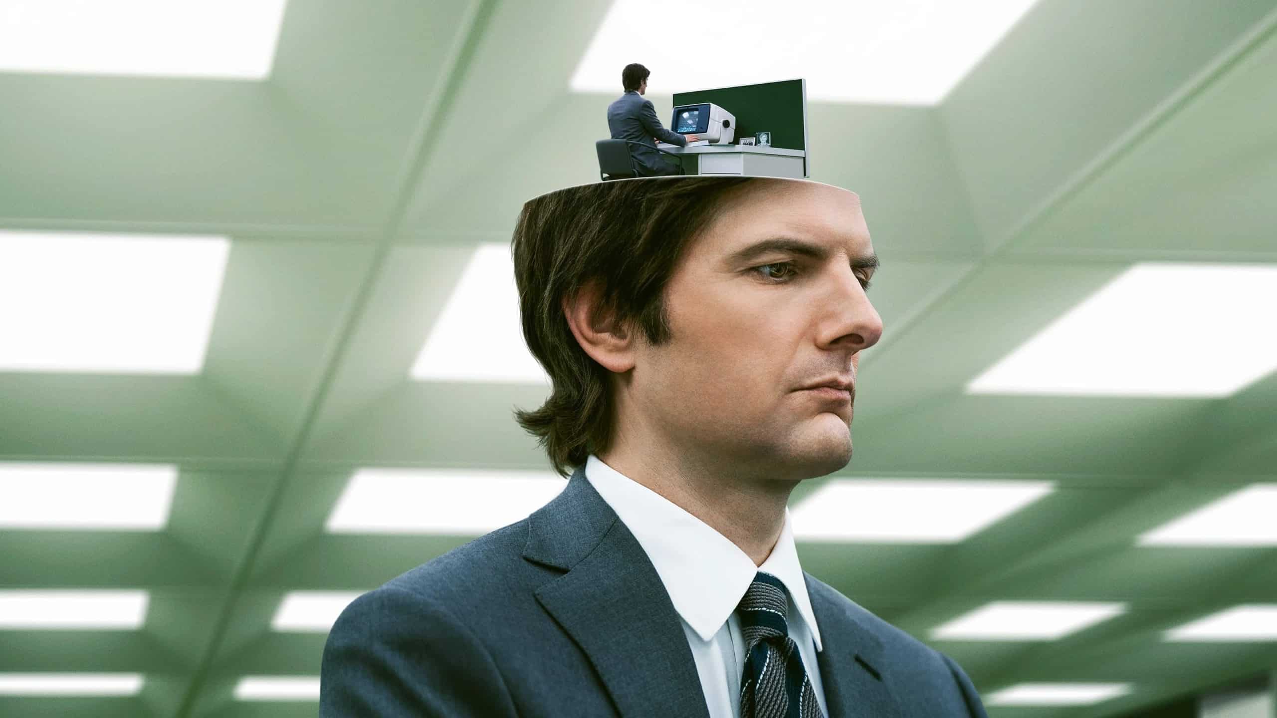 A man in a suit with a miniature version of himself working at a desk inside his head, from the show Severance.