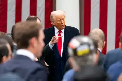 Donald Trump speaking to a crowd in front of a U.S. flag backdrop.