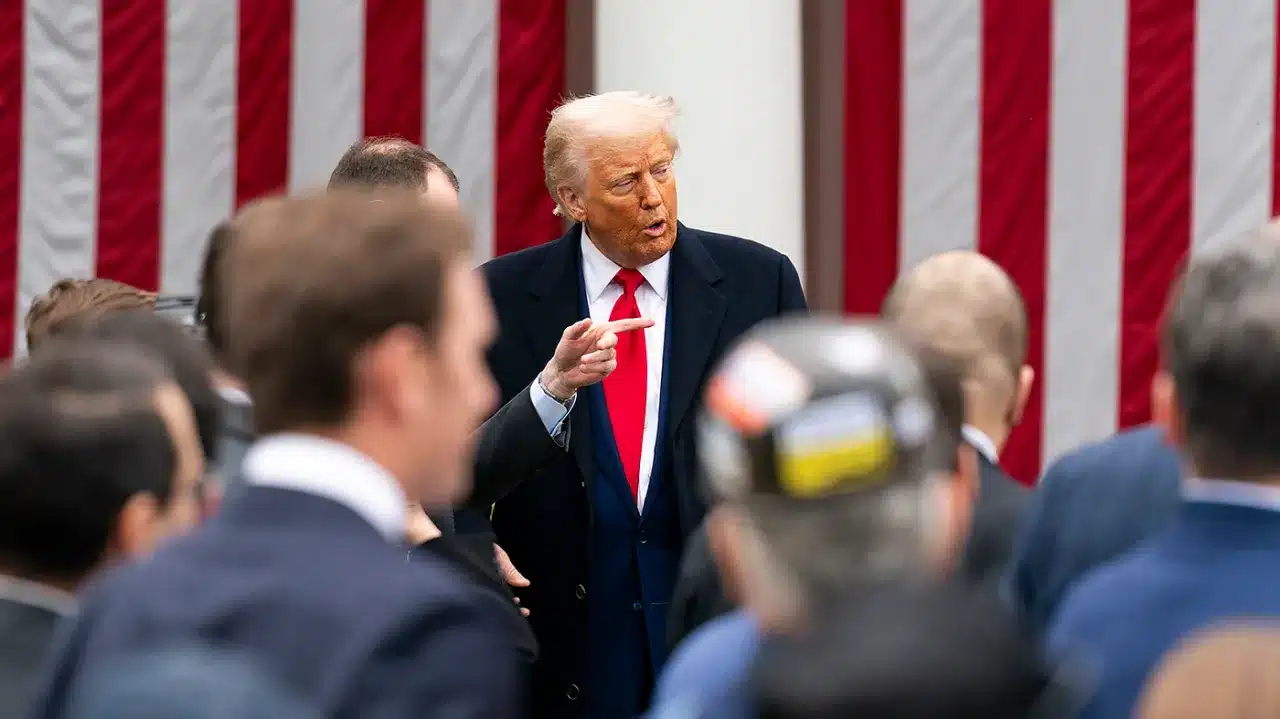 Donald Trump speaking to a crowd in front of a U.S. flag backdrop.