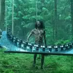 Film crew carries a curved rig of iPhones past a bloodied actor in a forest.