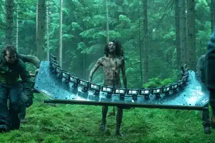 Film crew carries a curved rig of iPhones past a bloodied actor in a forest.
