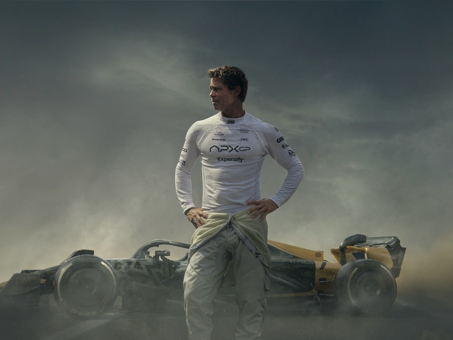 Brad Pitt stands in front of a Formula 1 race car in the movie F1.