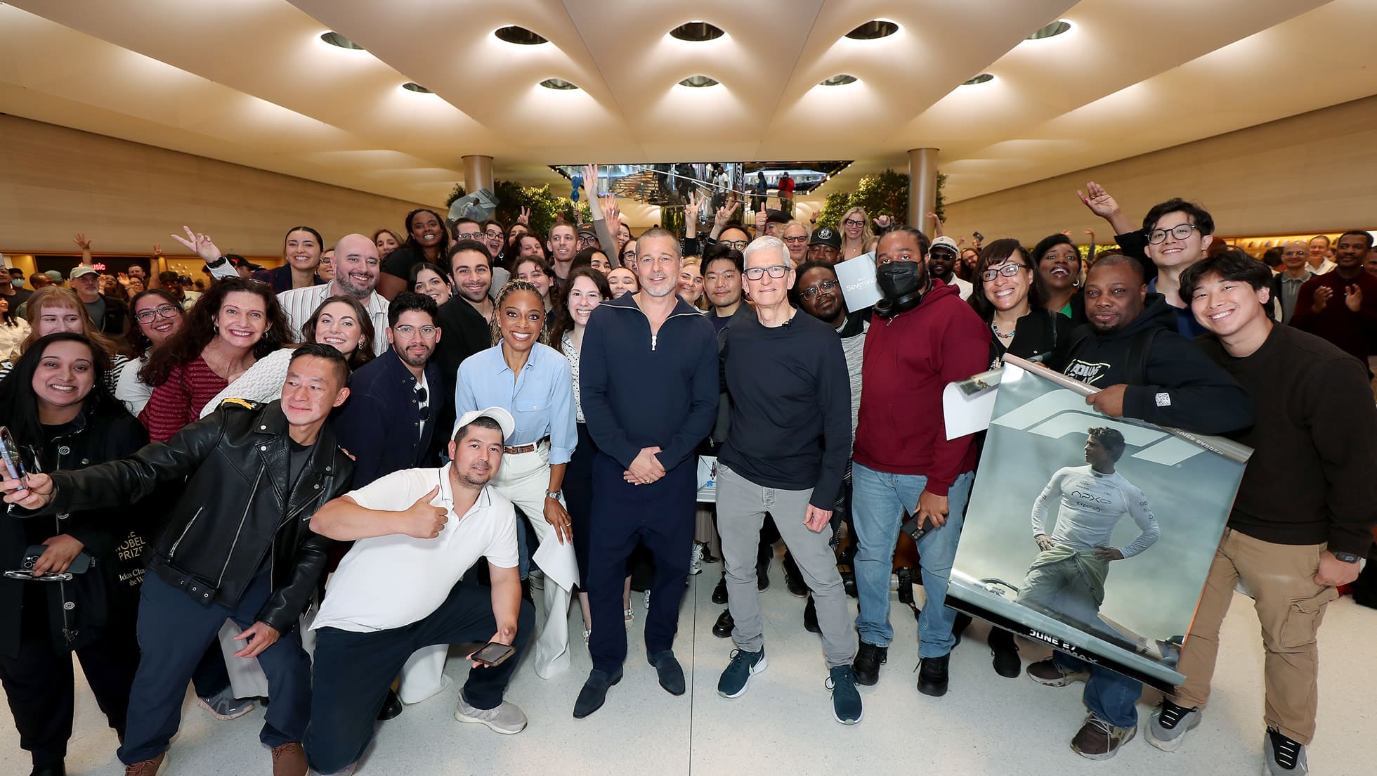Brad Pitt and Tim Cook standing amid a cheering crowd inside Apple Fifth Avenue during an F1 movie promotion.