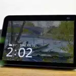 A tabletop smart display showing the time, date, and weather over a Van Gogh–style art wallpaper.