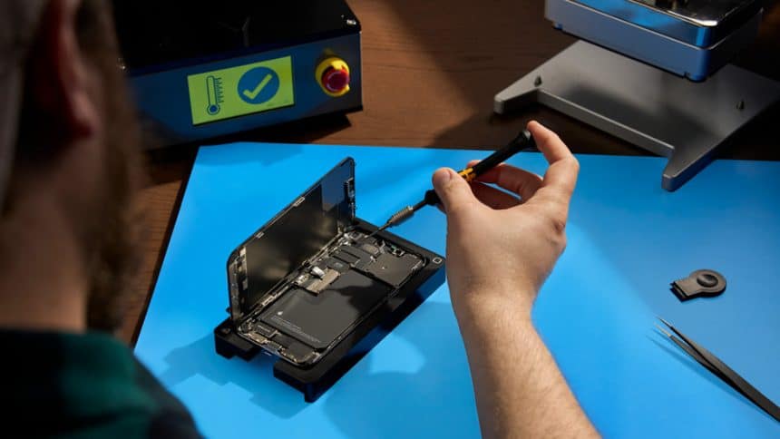 Technician unscrewing an open iPhone on a repair bench.