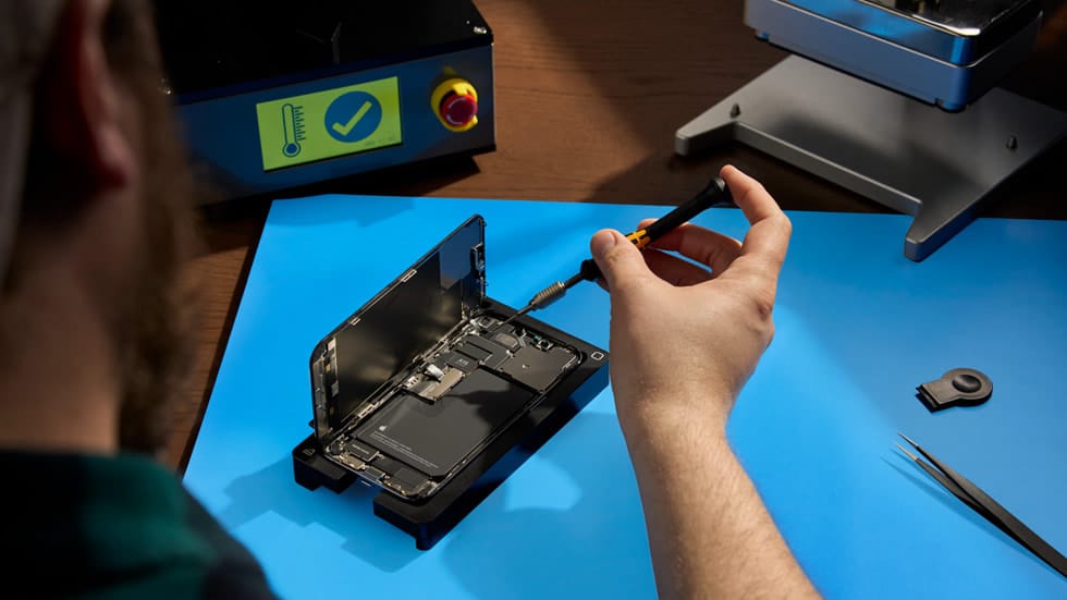 Technician unscrewing an open iPhone on a repair bench.