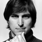 Black-and-white close-up portrait of Steve Jobs resting his chin on his hand.