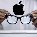A person holding Apple smart glasses with digital data reflections on the lenses.