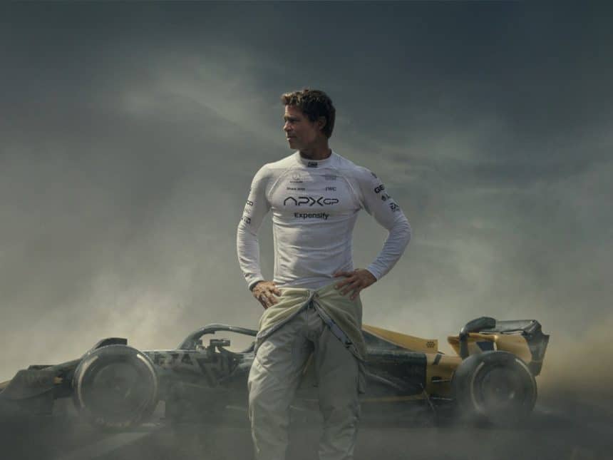 Brad Pitt in a racing suit standing in front of a Formula 1 car.
