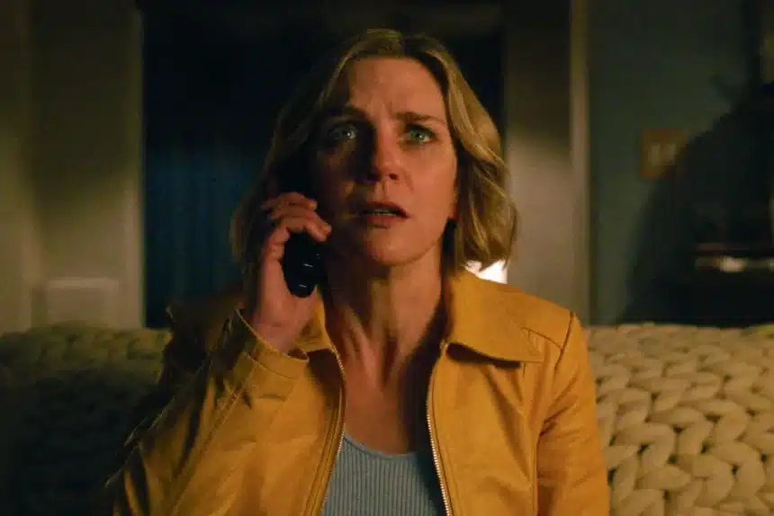 A woman in a yellow jacket looks shocked while talking on the phone.