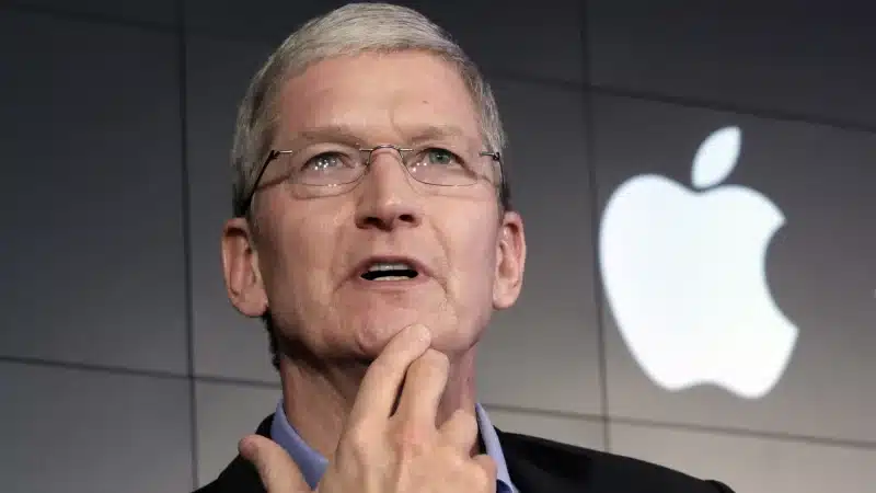 Tim Cook speaking at an Apple event with the Apple logo in the background.