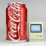 A tiny Macintosh replica next to a Coca-Cola can for size comparison.