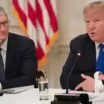 Tim Cook and Donald Trump speaking at a meeting with U.S. flags in the background.