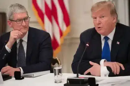 Tim Cook and Donald Trump speaking at a meeting with U.S. flags in the background.