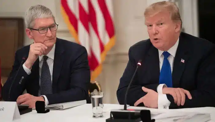 Tim Cook and Donald Trump speaking at a meeting with U.S. flags in the background.