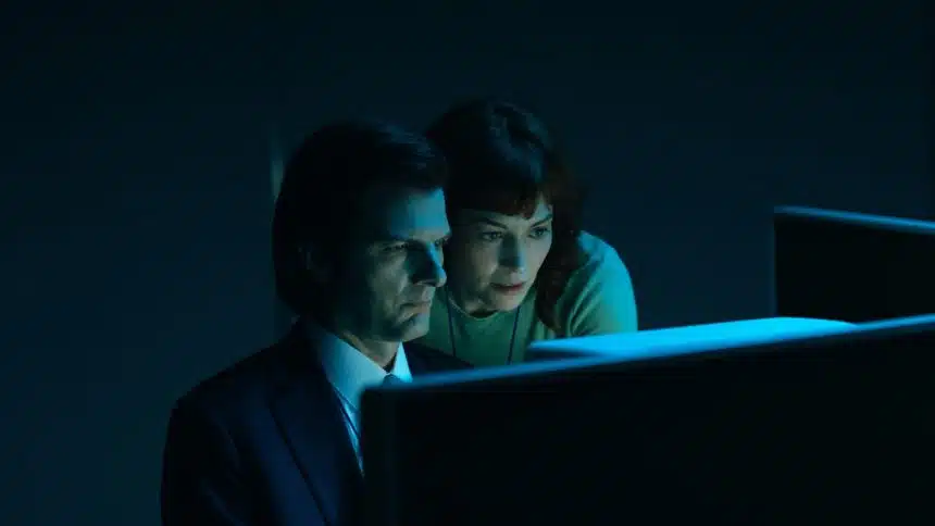 Two characters from Severance look at a glowing computer screen in a dark room.