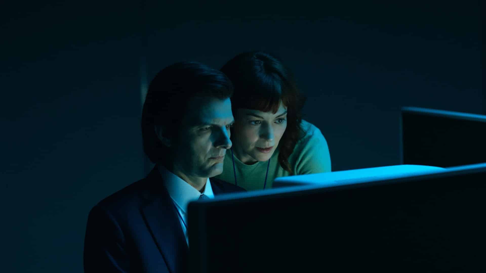Two characters from Severance look at a glowing computer screen in a dark room.
