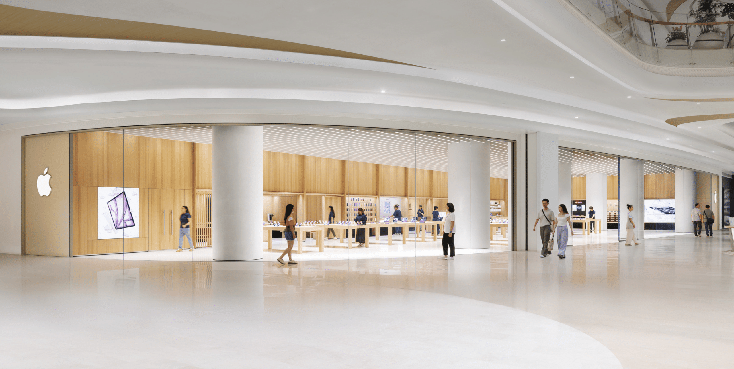 Apple Store in Shenzhen with glass walls, wood interior, and customers walking inside the mall.