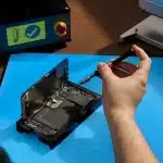 Person repairing an iPhone with precision tools on a blue work mat.