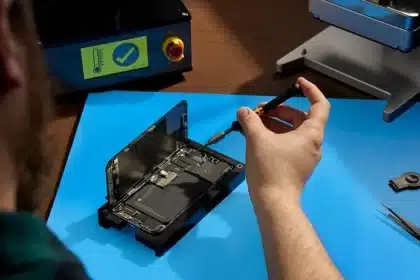 Person repairing an iPhone with precision tools on a blue work mat.