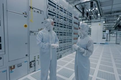 Two workers in protective suits inside a semiconductor manufacturing facility.