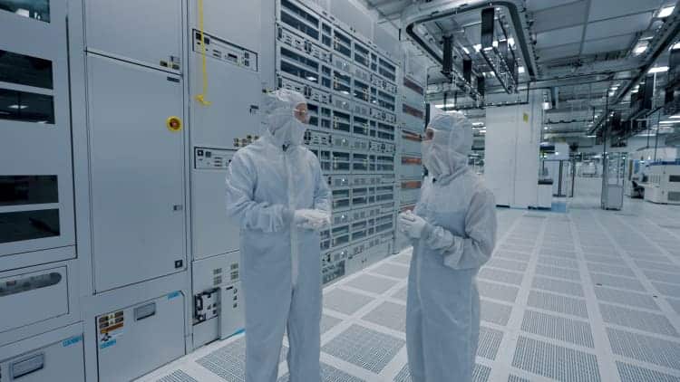 Two workers in protective suits inside a semiconductor manufacturing facility.