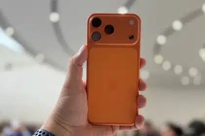 Hand holding an orange iPhone with a unique rear camera design.