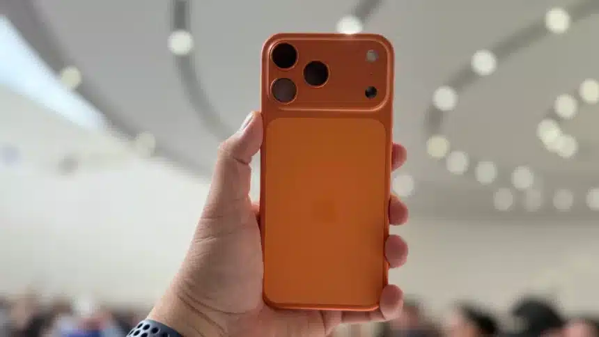 Hand holding an orange iPhone with a unique rear camera design.
